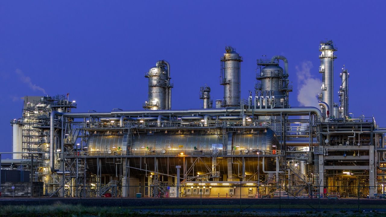 A striking view of an industrial facility in Zuid-Holland, illuminated at dusk against a clear blue sky.