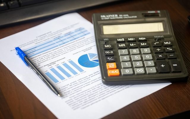 Close-up of a calculator, pen, and financial report on a wooden desk.