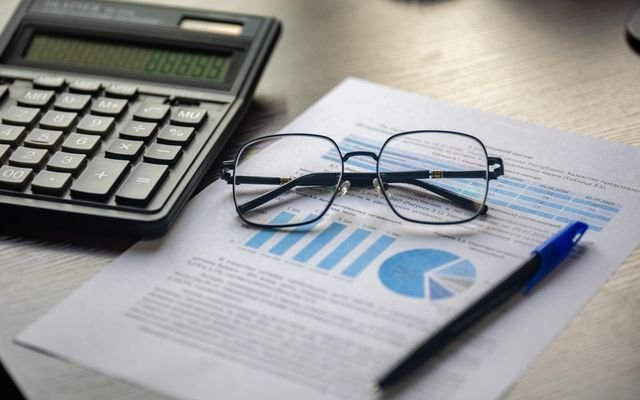 Financial document with a calculator, pen, and glasses symbolizing data analysis.