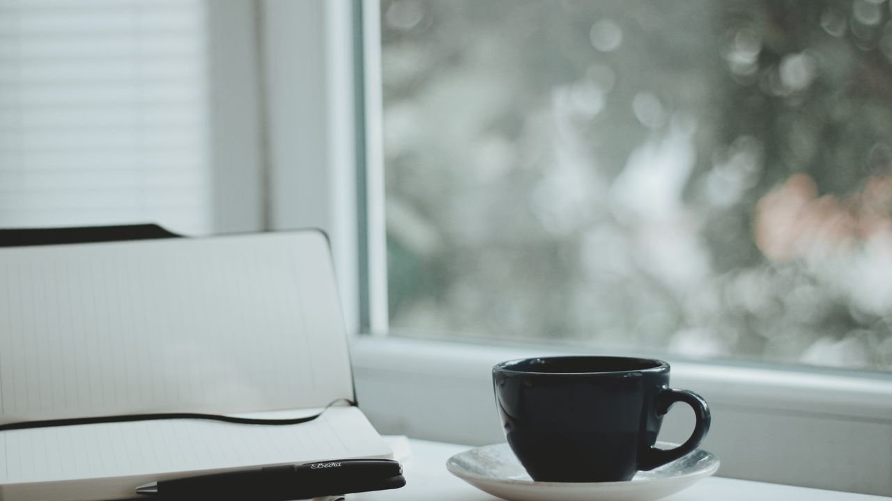 A serene scene with a coffee cup and notebook by a window, perfect for calm mornings.