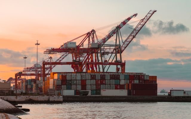 Container cranes at a bustling port during sunset, creating a vibrant industrial scene.