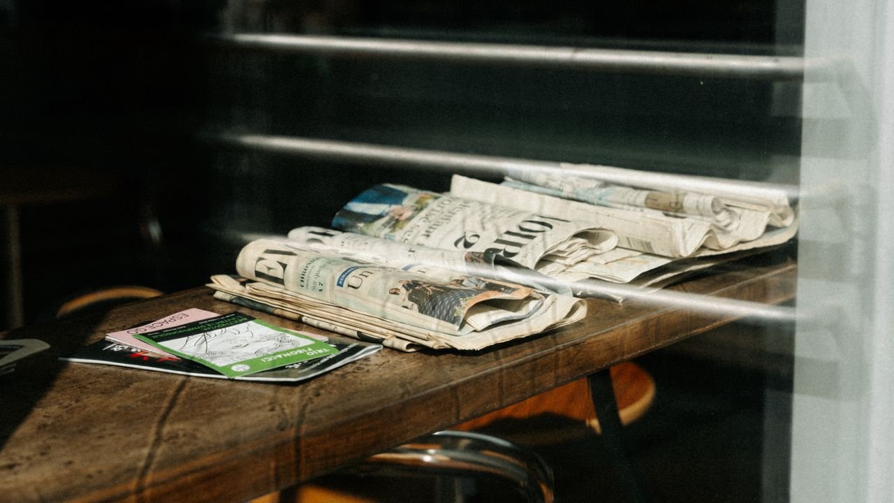 A stack of newspapers resting on a cafe table in Montreal, Quebec. Sunlight creating shadows.