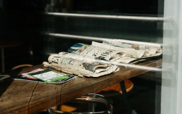 A stack of newspapers resting on a cafe table in Montreal, Quebec. Sunlight creating shadows.