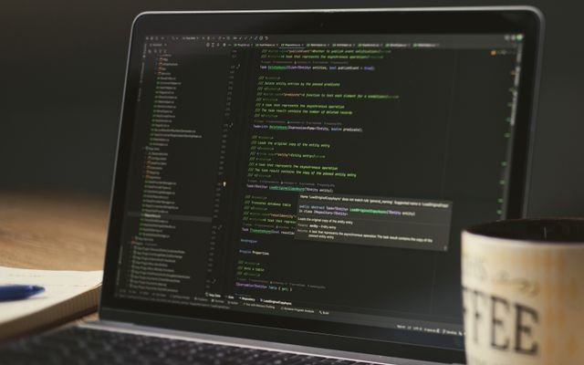 A close-up of a laptop displaying code in a dimly lit room with a coffee mug nearby.