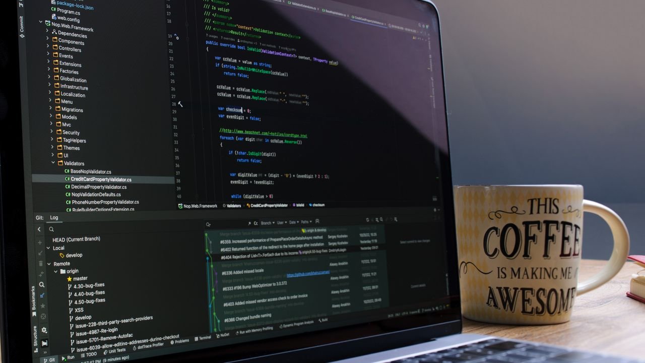 Close-up of laptop with coding software and a motivational coffee mug on a desk.