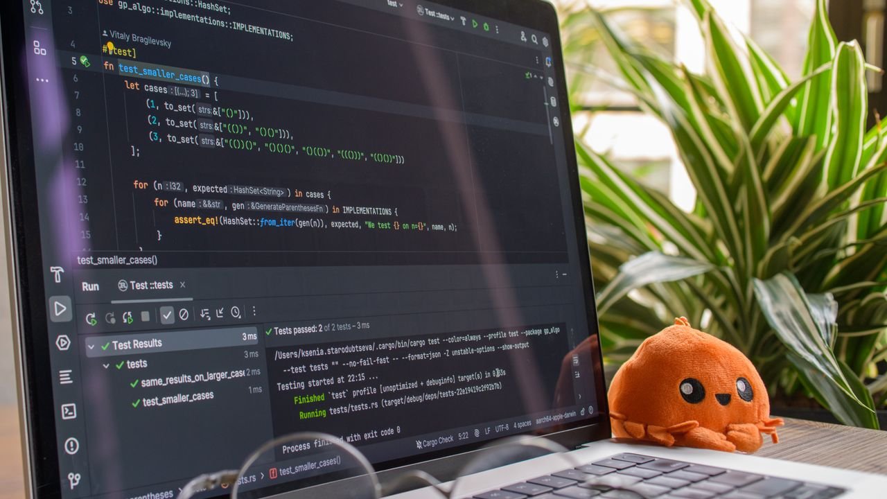A laptop displaying code in a modern indoor setting with an orange plush toy nearby.