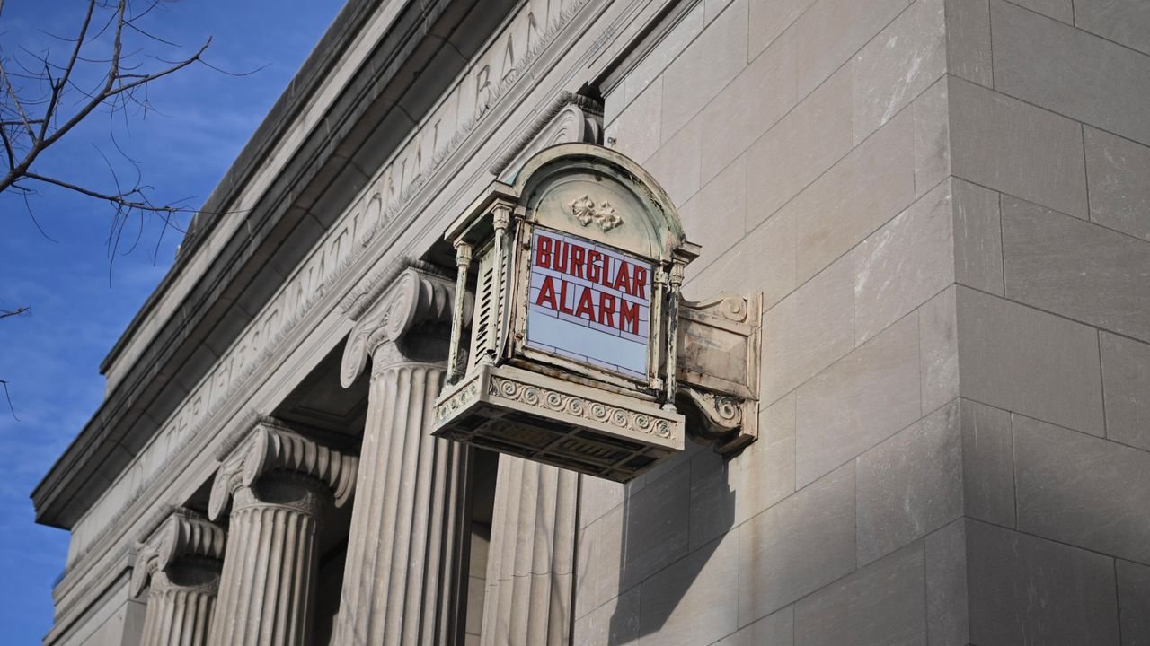A historical neoclassical building with a prominent burglar alarm sign.