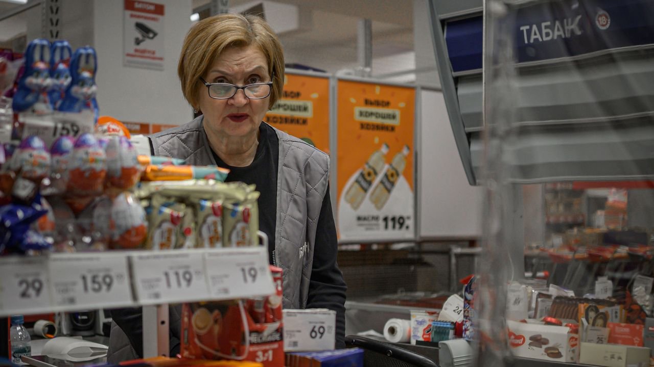Supermarket scene with cashier and assortment of products at checkout counter.