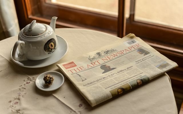 A serene indoor scene with a teapot, a newspaper, and a chocolate treat by the window.