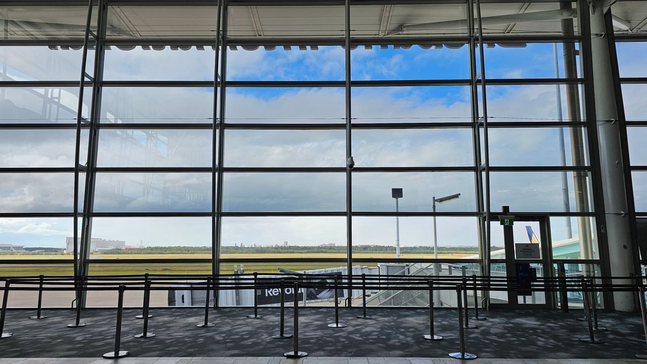 Large airport terminal with floor-to-ceiling windows offering a panoramic view of the sky and runway.