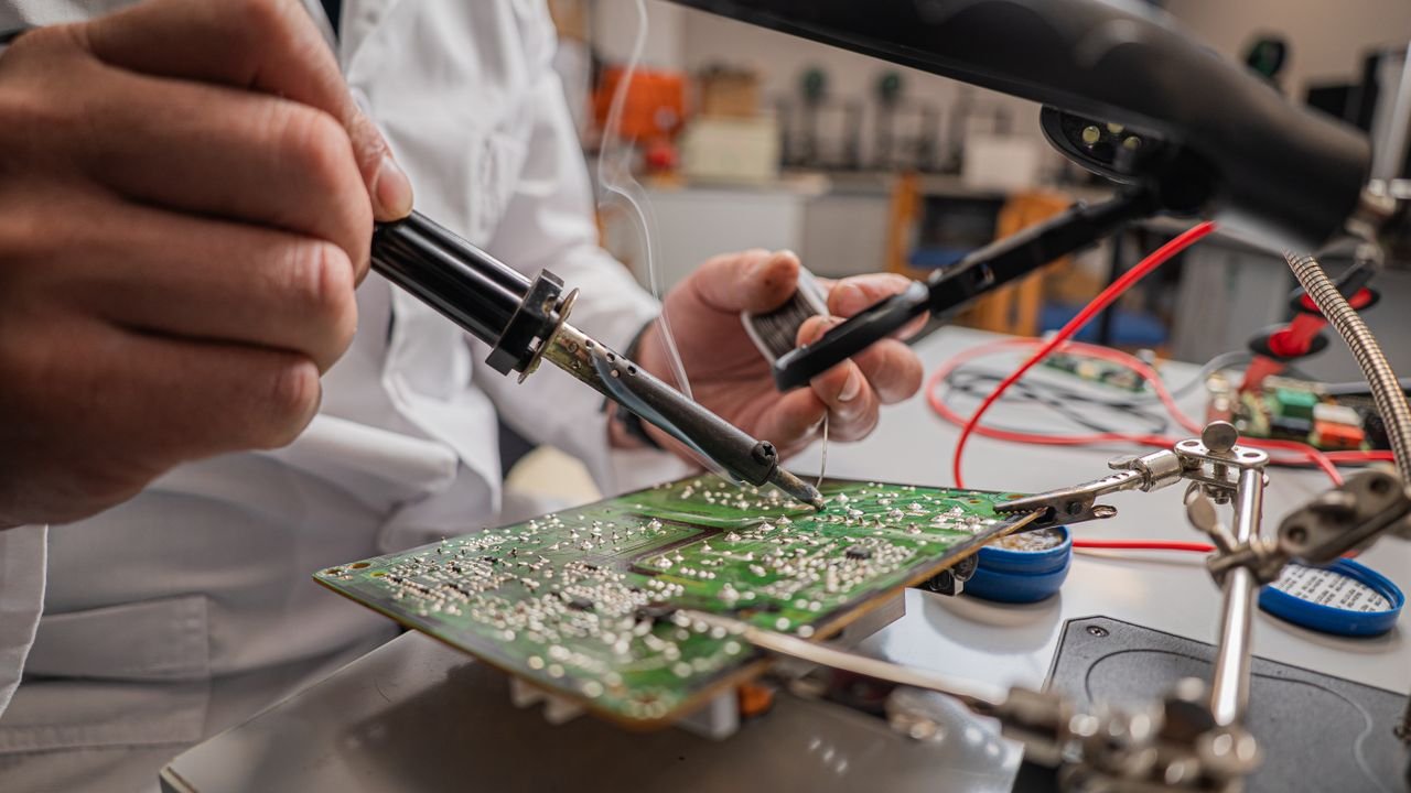 A skilled technician soldering electronic components on a green circuit board in a laboratory.
