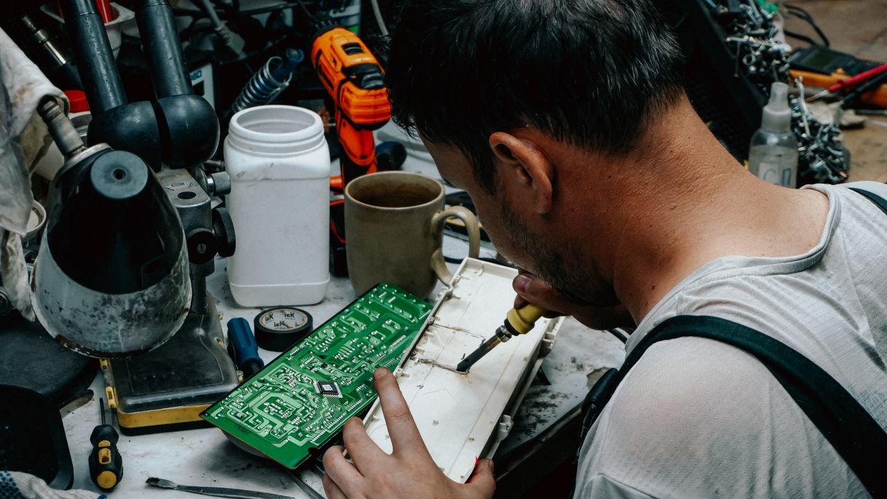 Close-up of a technician soldering a circuit board in a workshop, focusing on precise electronics work.