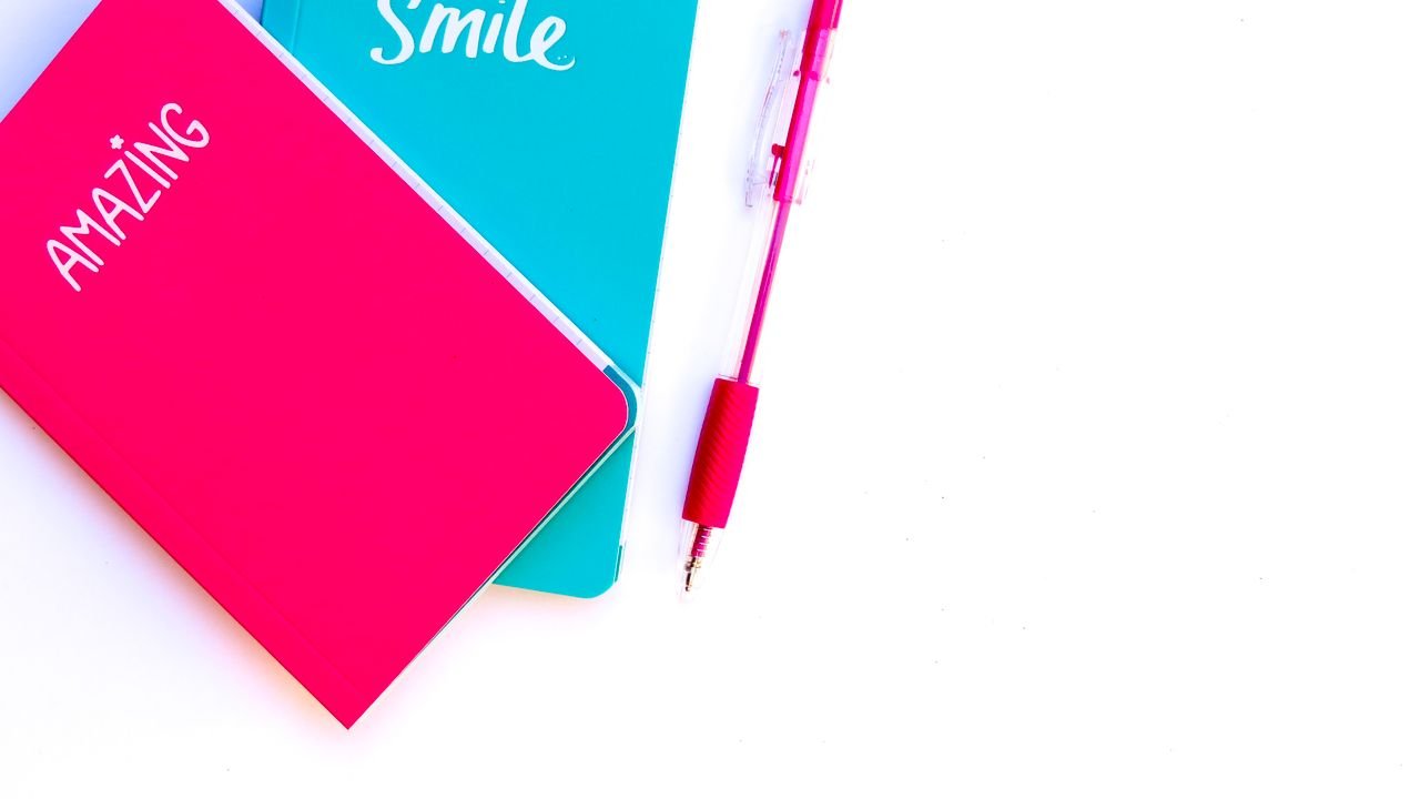 Colorful flat lay with turquoise and pink notebooks and matching pen on white background.