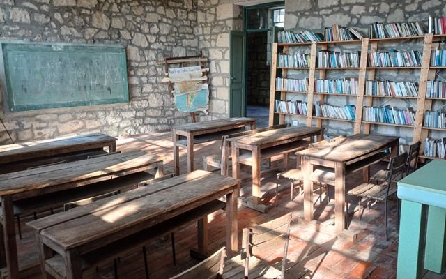 Vintage classroom with wooden desks, blackboard, and bookshelves.