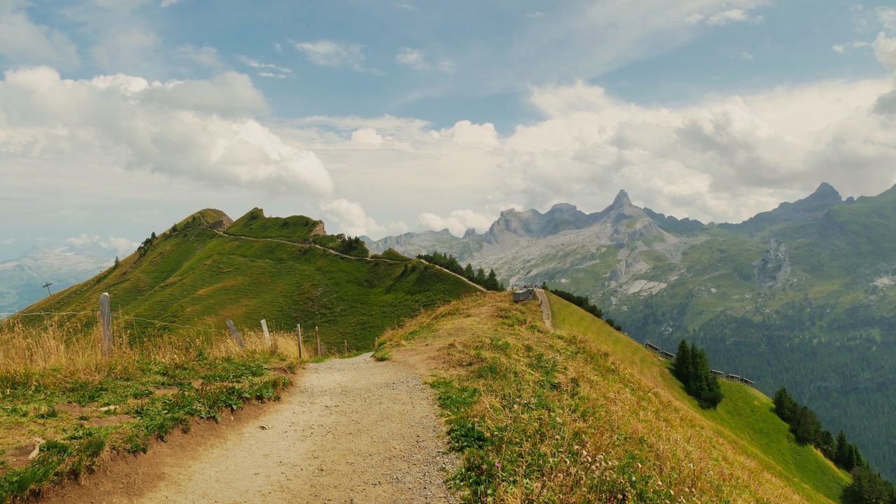 Discover a scenic hiking trail with stunning views of the Swiss Alps under a clear blue sky.