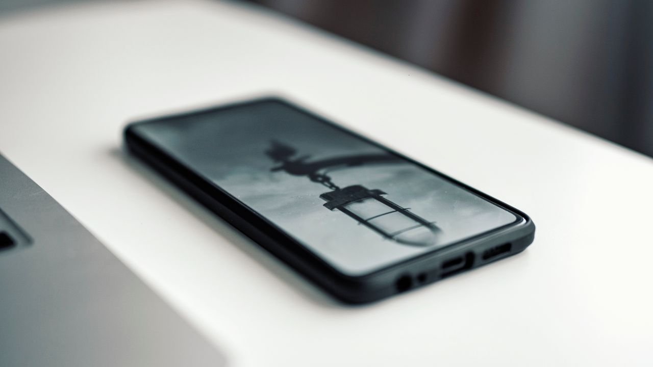 Close-up of a smartphone displaying a blurred image, placed on a desk beside a laptop.