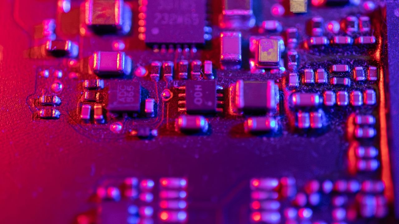 Macro shot of an electronic circuit board with vivid purple and pink lighting, highlighting components.