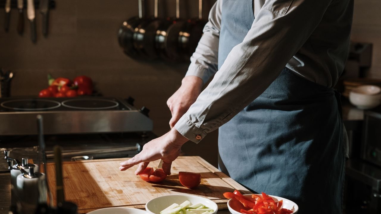 Chef slicing fresh tomatoes and peppers on a wooden board in the kitchen.