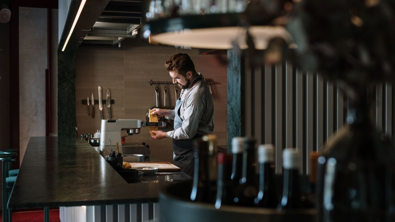 A male chef meticulously prepares a dish in a contemporary restaurant kitchen, surrounded by culinary tools.