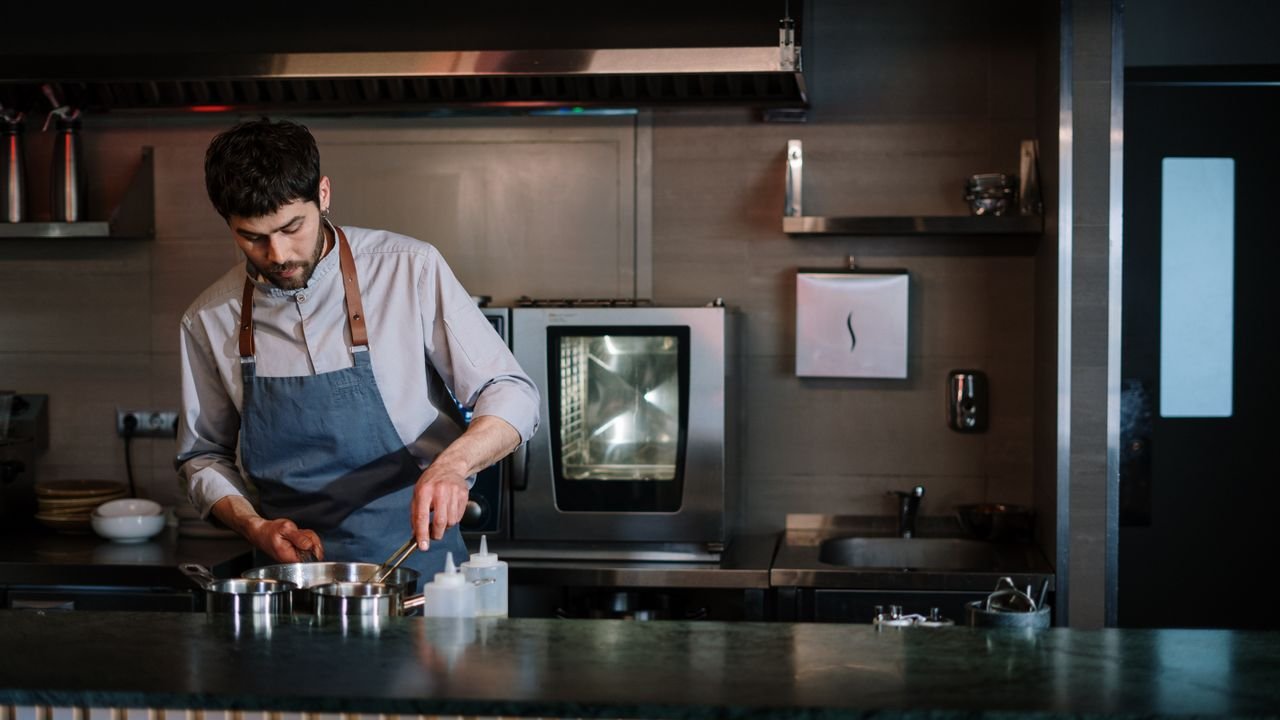 A chef in a blue apron cooking at a modern open kitchen counter.