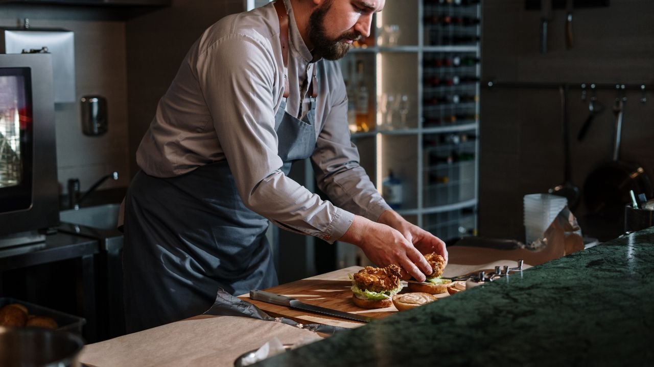 Chef preparing a gourmet beef burger with precision in a modern kitchen setting.
