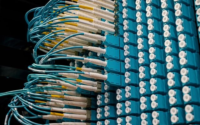 Detailed view of fiber optic patch cables connecting to a blue patch panel in a data center.