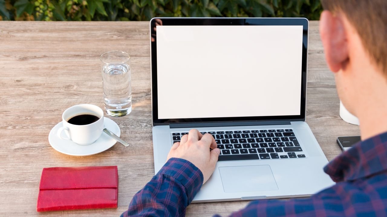 Adult working on laptop outdoors with coffee and notepad, promoting remote work flexibility.