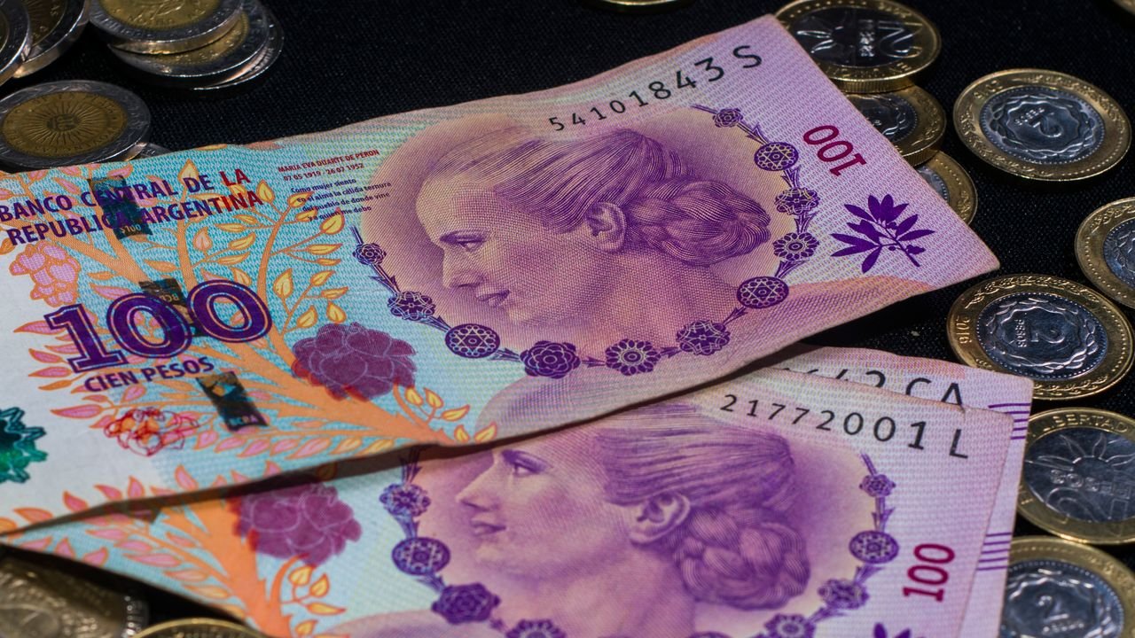 Close-up of colorful Argentine peso banknotes and coins on a dark backdrop.