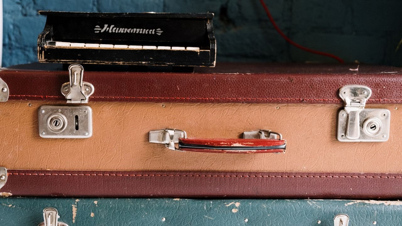 Stack of vintage suitcases topped with an antique harmonium music box against a brick wall.