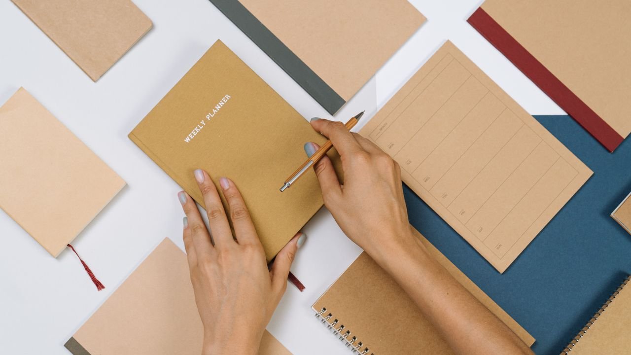 Organized flat lay of stationery items with hands writing in a planner, suitable for productivity themes.