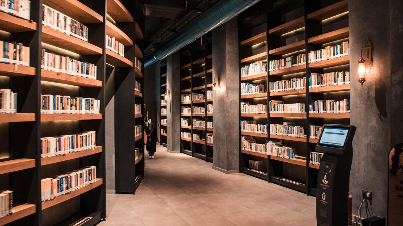 A spacious library featuring tall wooden bookshelves filled with books and ambient lighting.