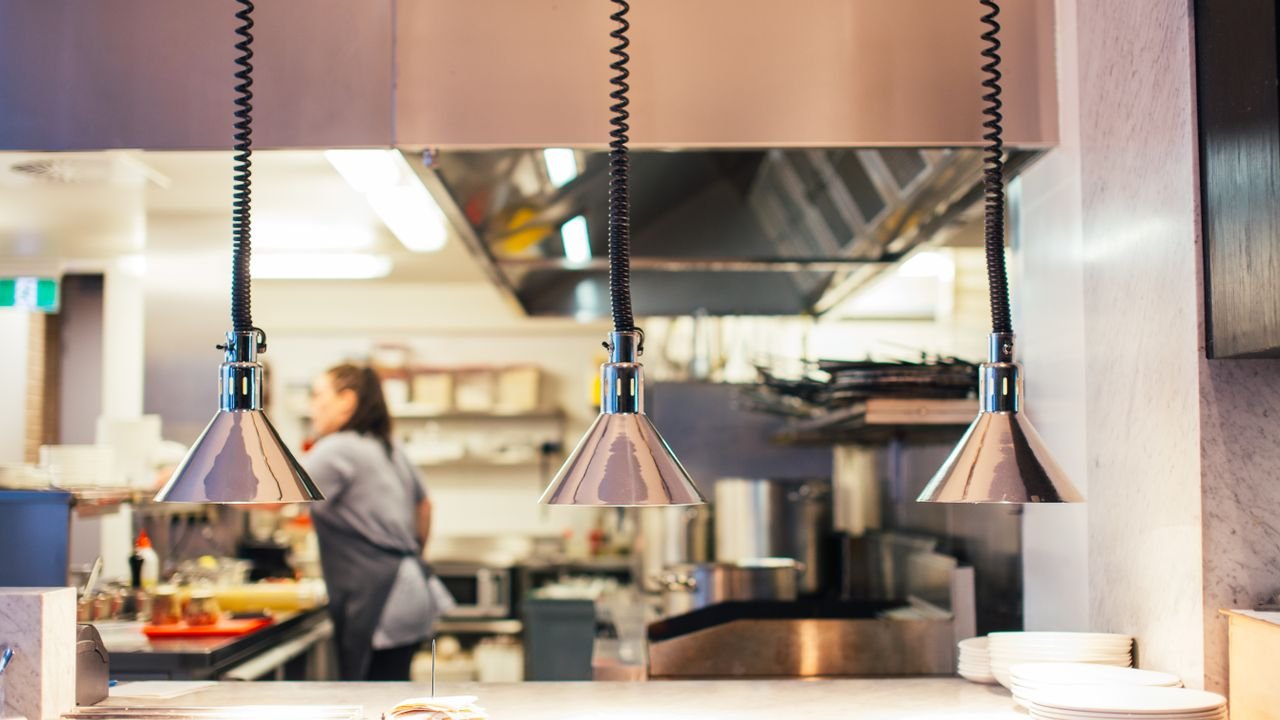 Side view of unrecognizable female chef in restaurant kitchen working behind counter with infrared lamps and serving kitchenware