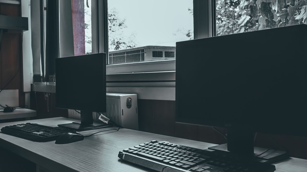 Contemporary computers with black screens placed on desk near window in classroom or office
