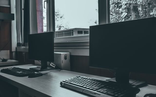 Contemporary computers with black screens placed on desk near window in classroom or office