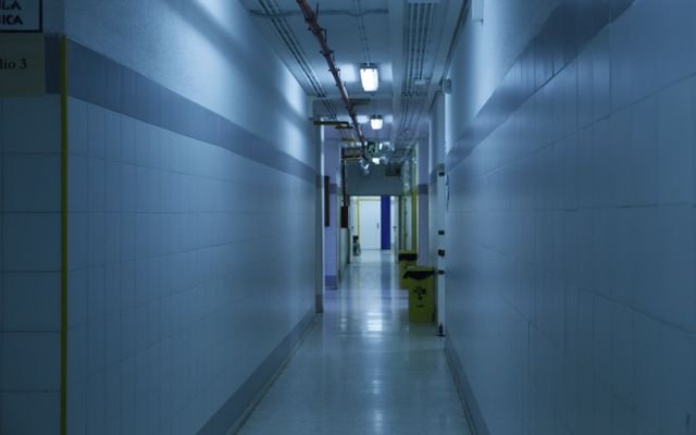 A deserted, dimly lit hallway with tiled walls and overhead lights.