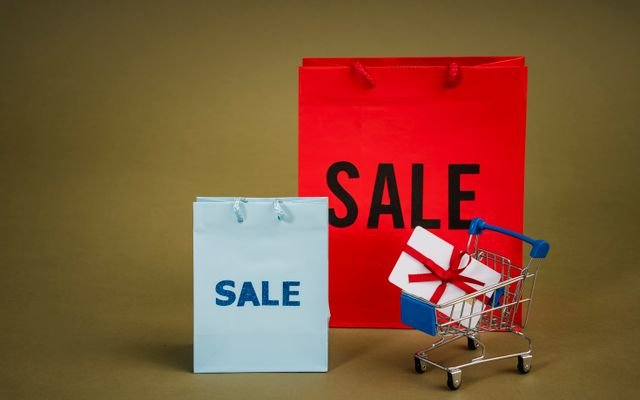 Bright sale bags with a gift in a shopping cart against a neutral background.