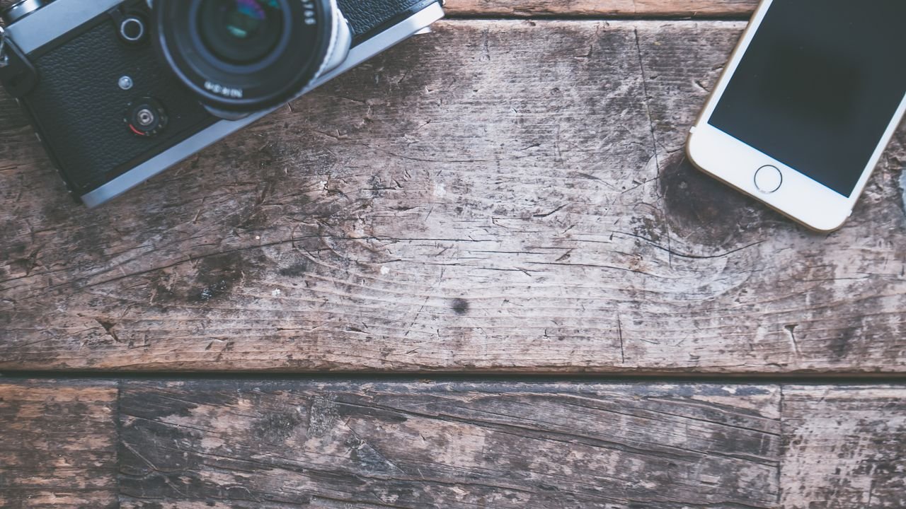 A flat lay of a vintage camera and smartphone on a rustic wooden table, ideal for tech and photography themes.