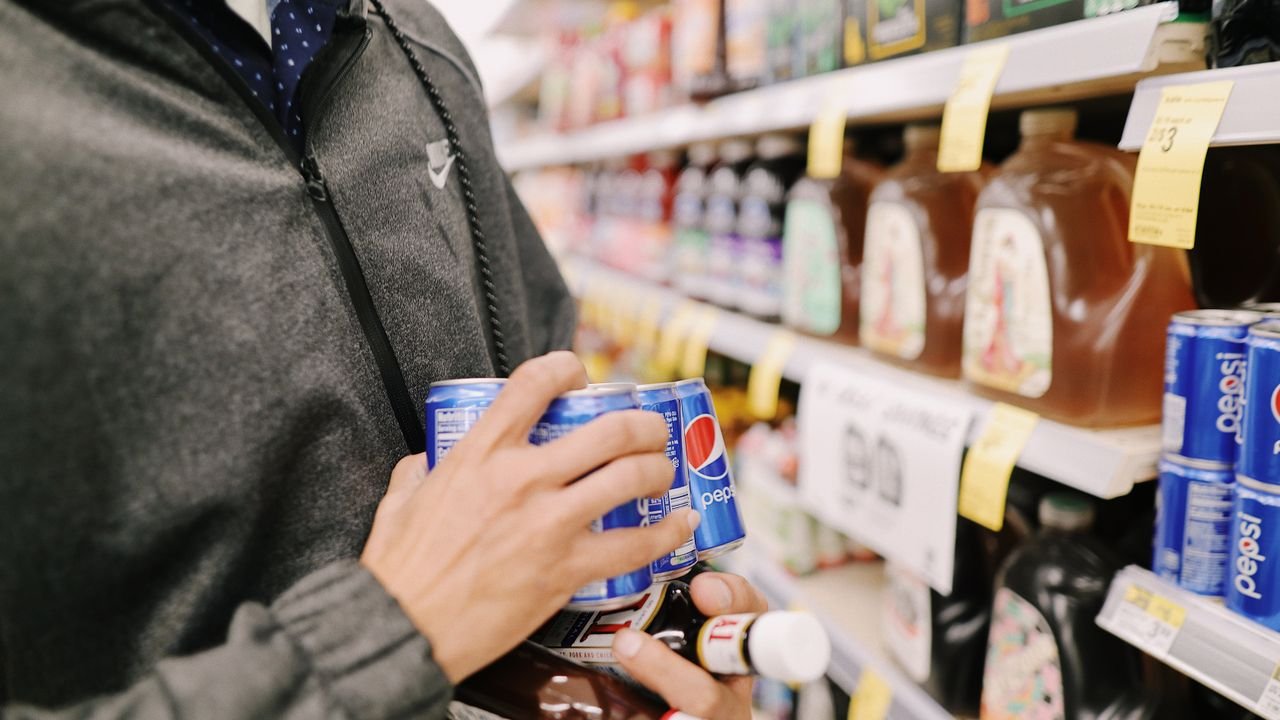 Close-up of an adult shopping for Pepsi and sauces in a grocery store aisle.