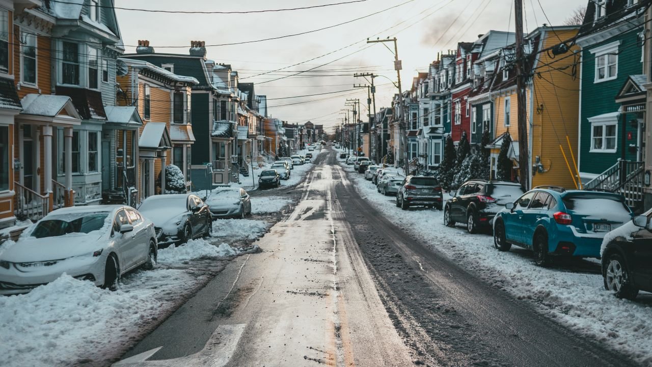 Asphalt roadway with snow and arrow between parked automobiles and dwelling building facades on winter day