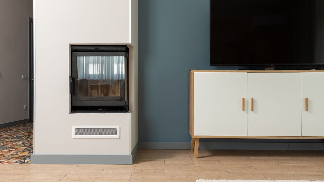 Modern design of contemporary apartment with big TV set placed on white stand near fireplace mounted in construction box