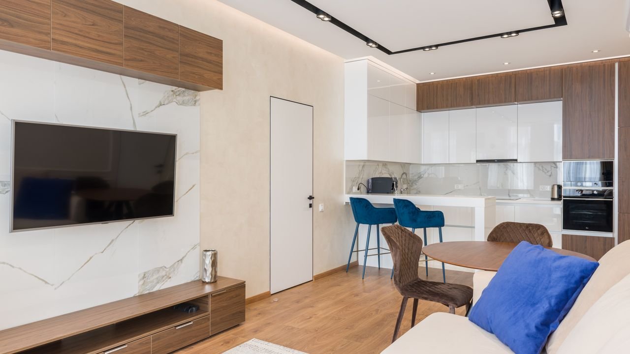 Interior of living room and open kitchen with comfortable sofa TV and chairs placed near round table in modern apartment