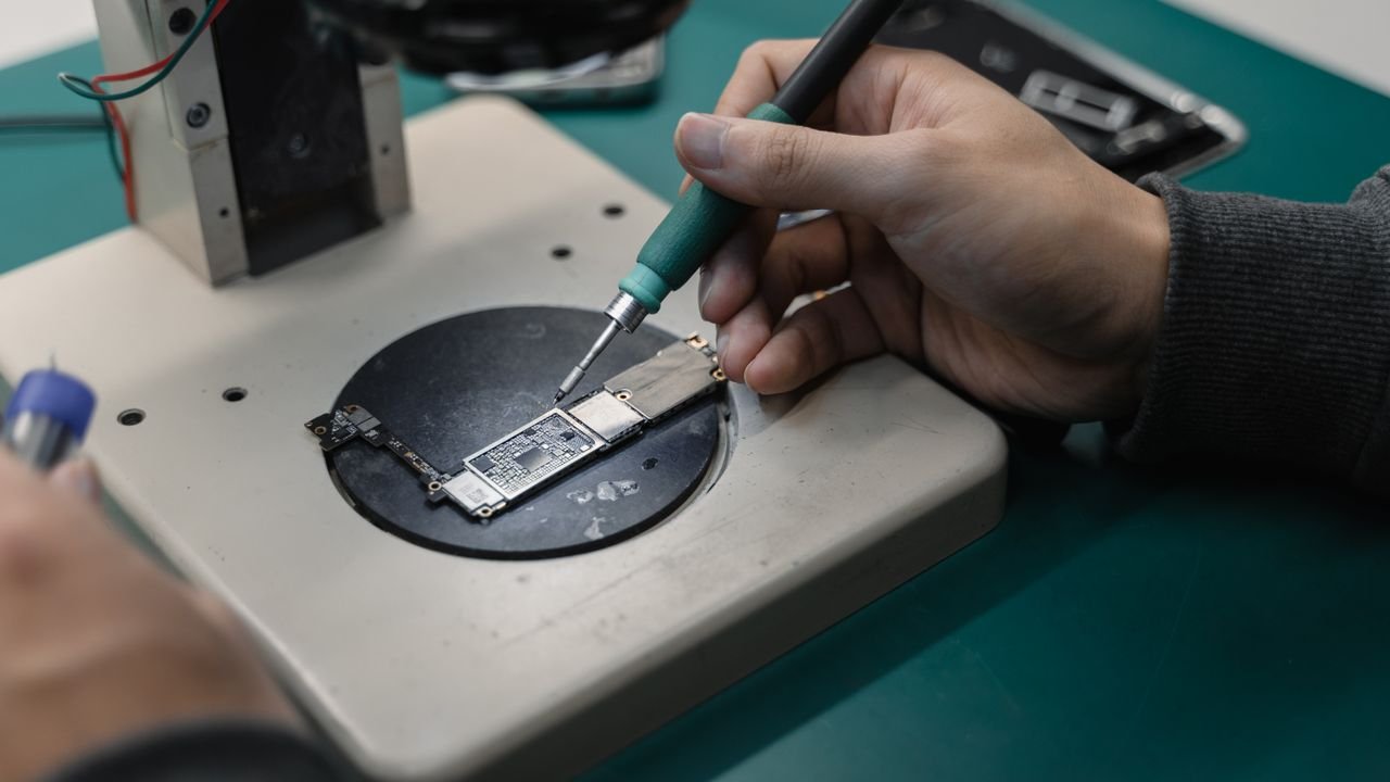 Detail view of hands soldering a circuit board in an electronics workshop.