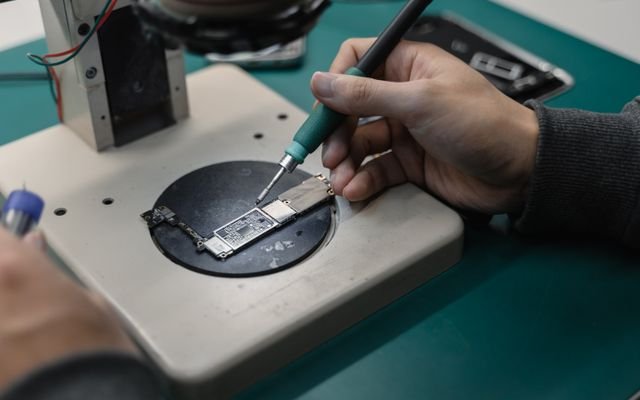 Detail view of hands soldering a circuit board in an electronics workshop.