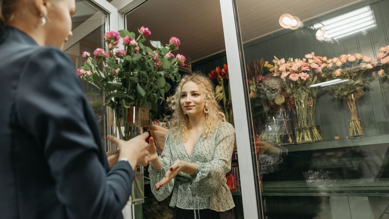 A flower shop owner hands a bouquet to a customer indoors.