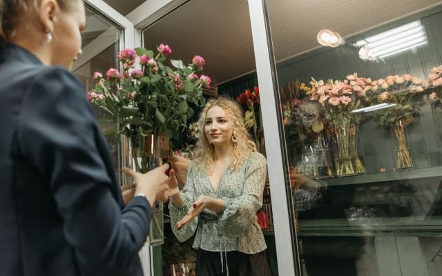 A flower shop owner hands a bouquet to a customer indoors.