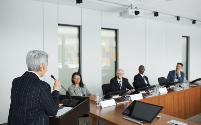 A diverse group of professionals engaging in a business meeting in a conference room with a speaker at the podium.