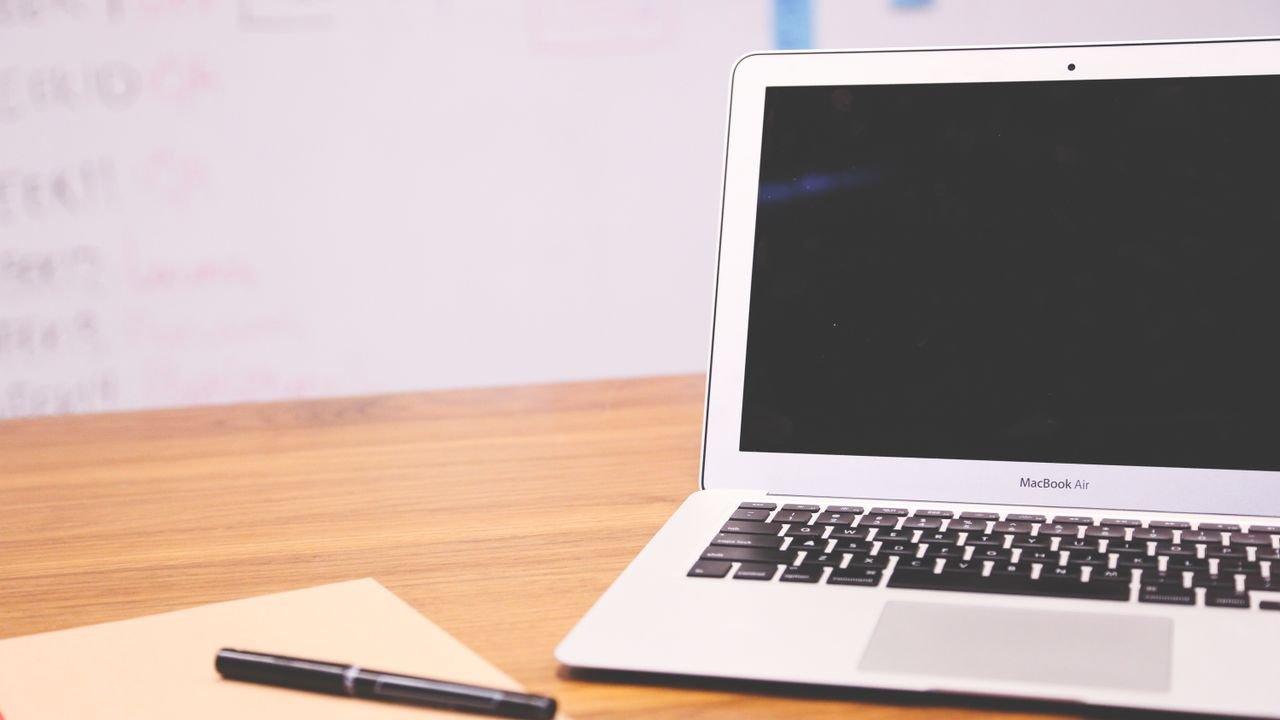 Sleek laptop on wooden desk with pen and notepad, ideal for business and tech settings.