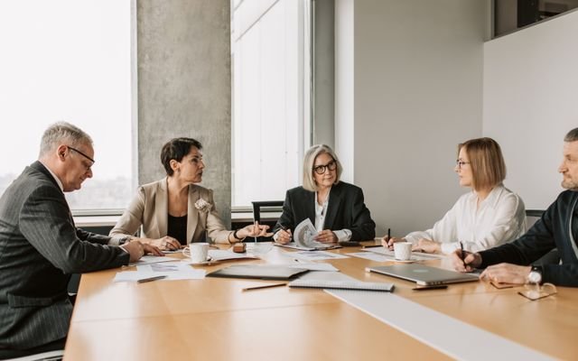 Five business professionals engaged in a meeting in a modern office setting, discussing documents and ideas.