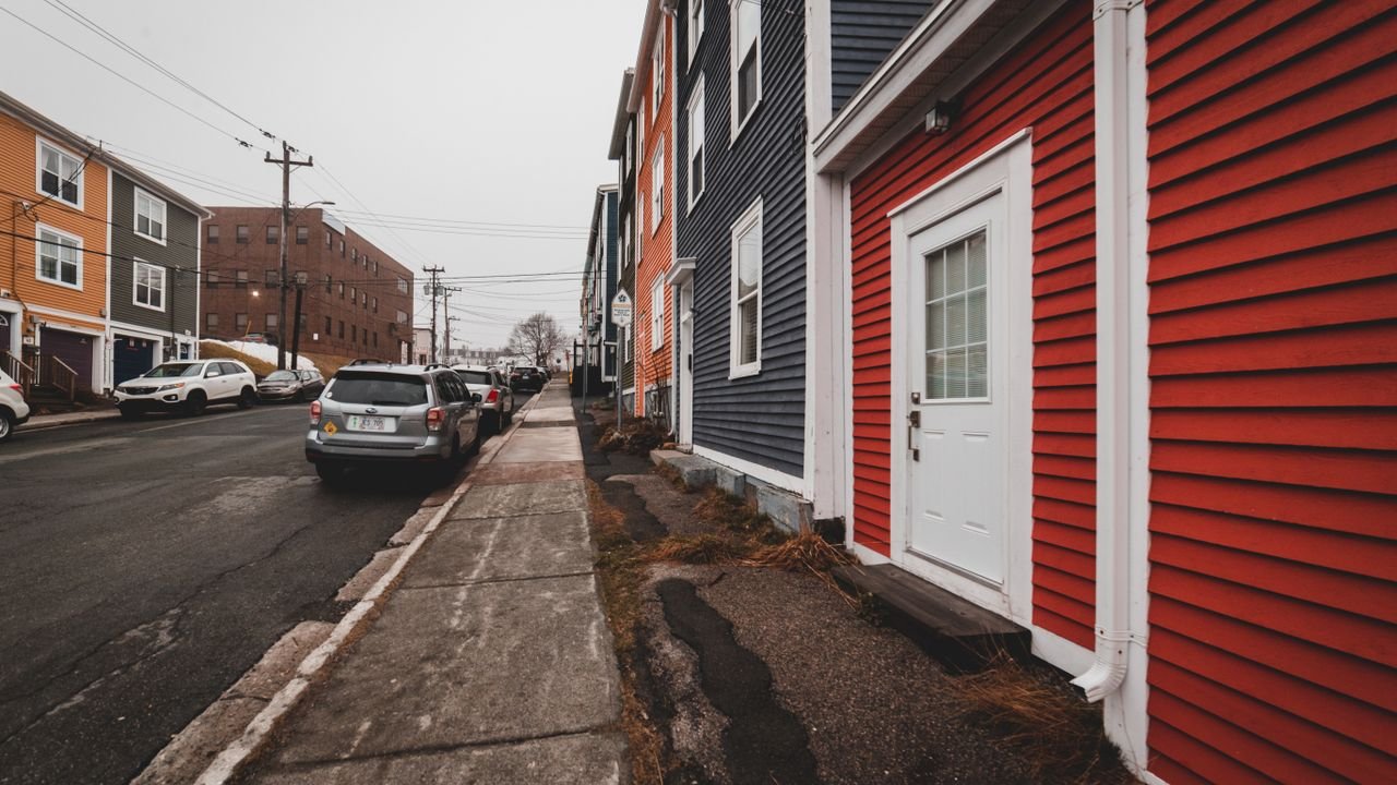 Bright old fashioned residential houses with windows located near asphalt roadway with modern cars on street of town against cloudless sky
