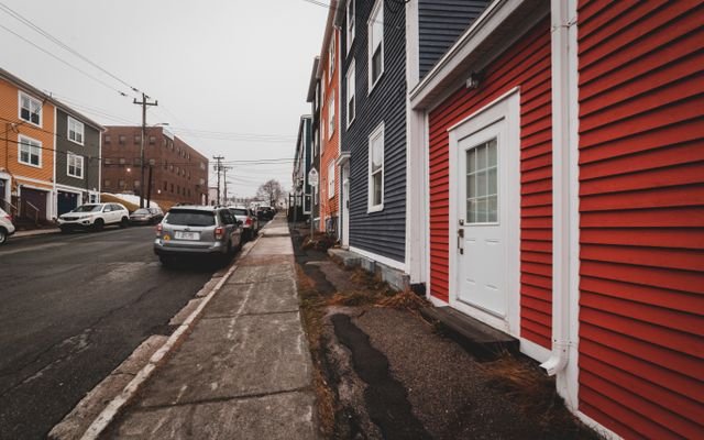 Bright old fashioned residential houses with windows located near asphalt roadway with modern cars on street of town against cloudless sky